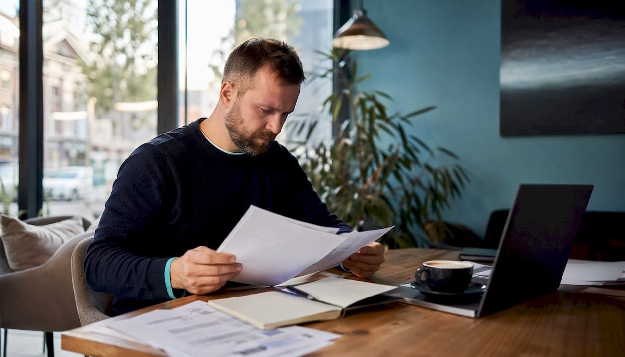 Vyras prie darbo stalo kruopščiai tikrina finansinių technologijų atitikties dokumentus.